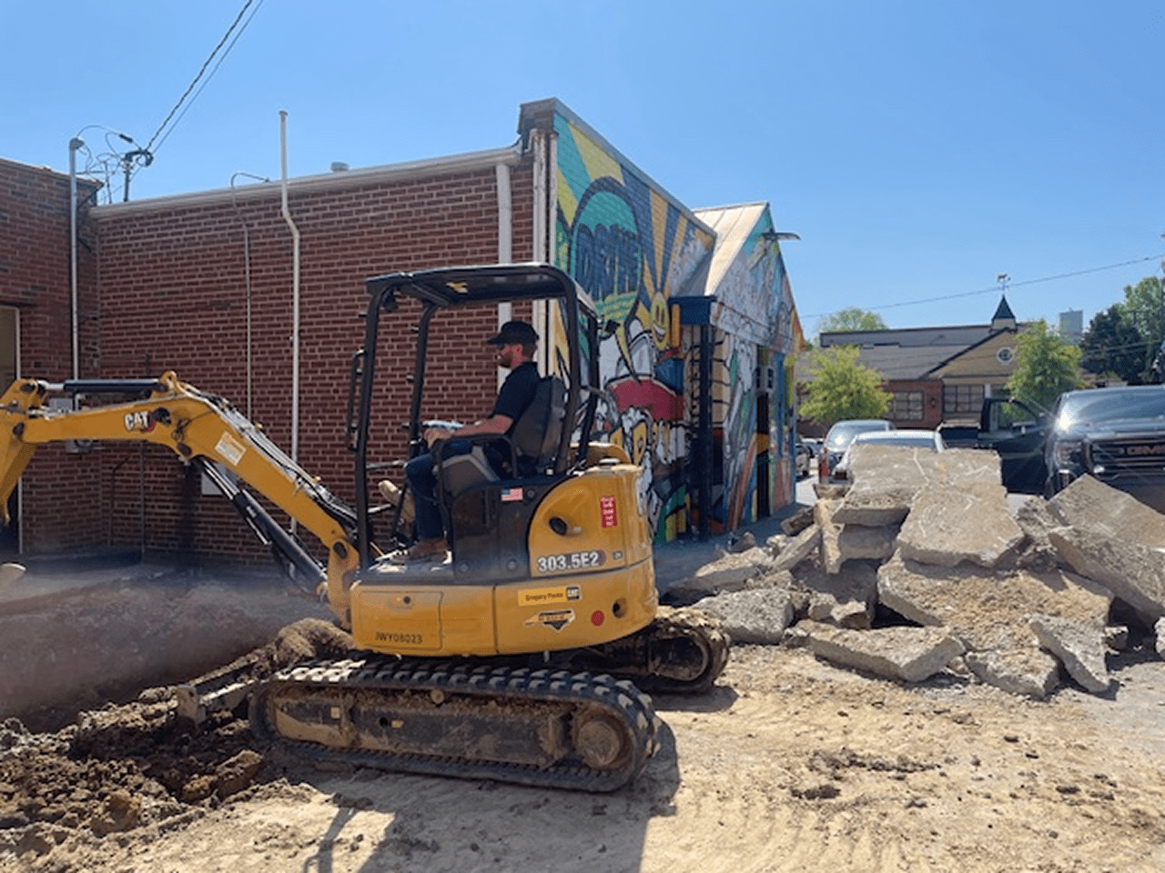 Worker operating excavator by brick building.